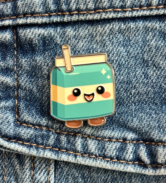 A cute kawaii-style enamel pin shaped like a smiling cool milk carton with a straw, shown pinned onto blue denim fabric.
Copyright © Cute Bites® All rights reserved.